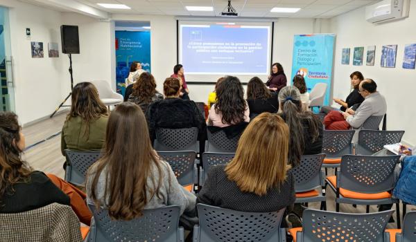 Grupo de personas reunidas en una sala donde se está realizando una presentación
