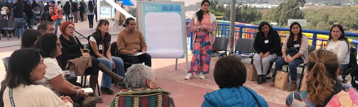 Grupo de personas sentadas en círculo escuchando a mujer que expone