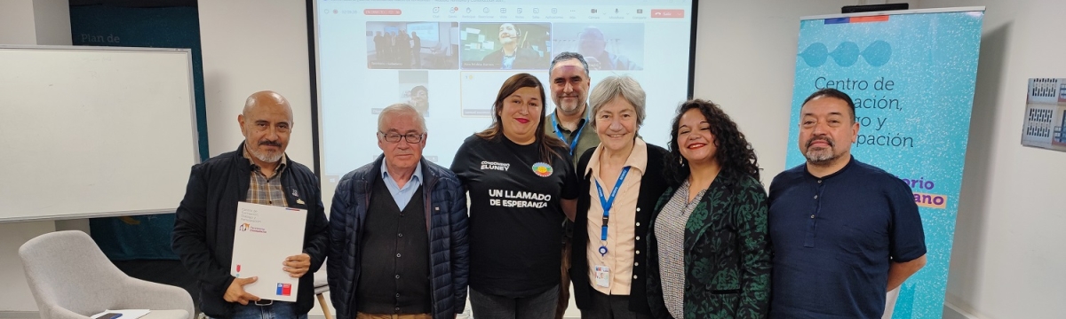 Grupo de personas frente a proyección de reunión mirando a cámara