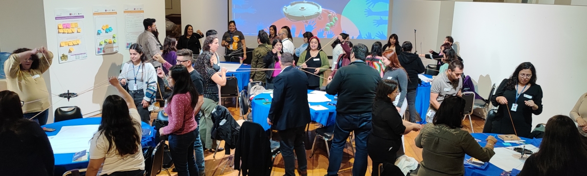 Muchas personas reunidas alrededor de mesas realizando un ejercicio colaborativo de coordinación