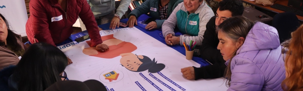 Grupo de personas de pie y sentadas alrededor de una mesa trabajando en un papelógrafo