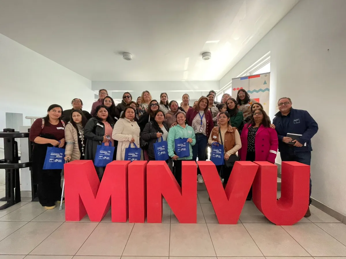 Grupo de personas de pie detrás de letras grandes que conforman la sigla MINVU