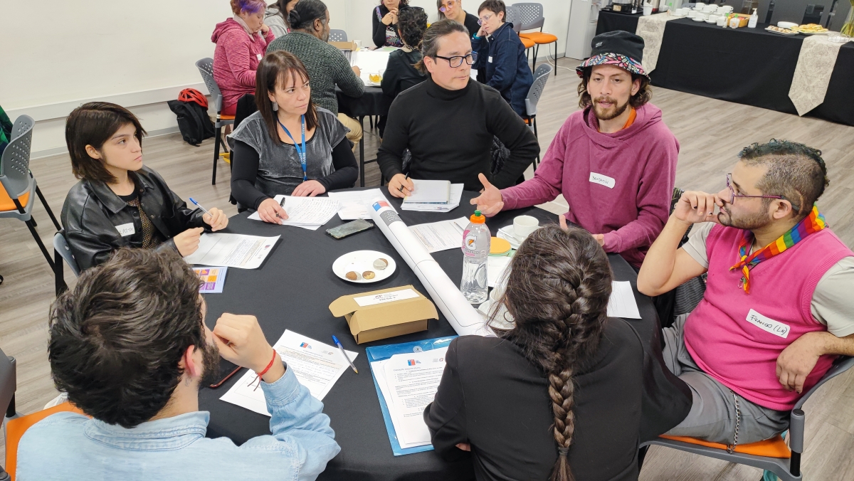 Un grupo de personas conversan sentados en una mesa redonda