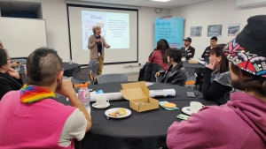 Un mujer expone ante una sala con personas sentadas en mesas redondas