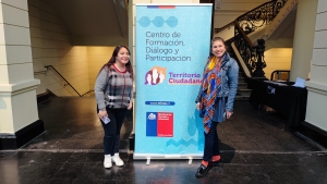 Dos mujeres posan al lado de pendón del Centro de Formación, Diálogo y Participación