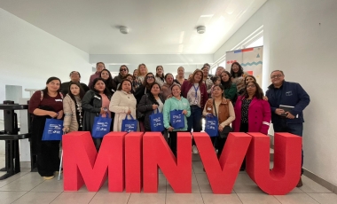 Grupo de personas de pie detrás de letras  grandes que conforman la sigla MINVU