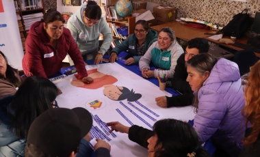 Grupo de personas de pie y sentadas alrededor de una mesa trabajando en un papelógrafo