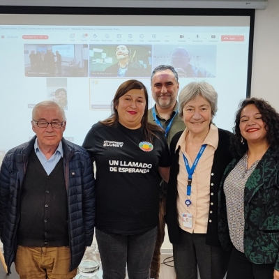 Grupo de personas frente a proyección de reunión mirando a cámara