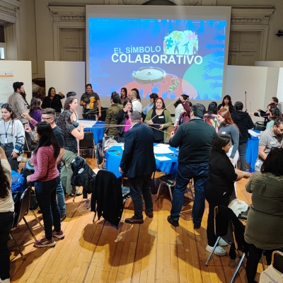 Muchas personas reunidas alrededor de mesas realizando un ejercicio colaborativo de coordinación